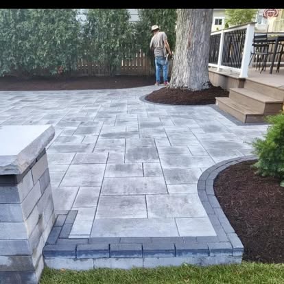 A large gray paver patio with a seat wall set around a mature tree.
